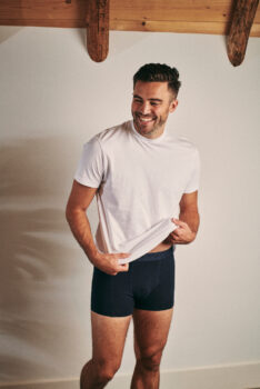 Man wearing a dark boxers of Suitable and a basic T-shirt, smiling away from the camera.